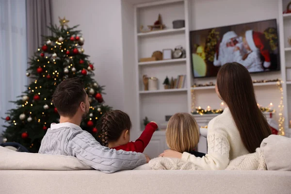 Family watching Christmas movie via TV in cosy room, back view. Winter holidays atmosphere