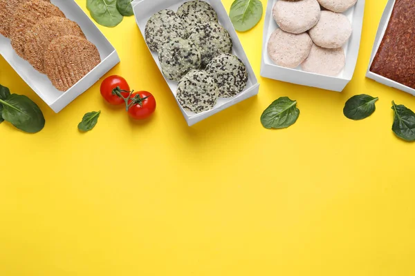 Many different raw vegan meat products, tomatoes and spinach on yellow background, flat lay. Space for text