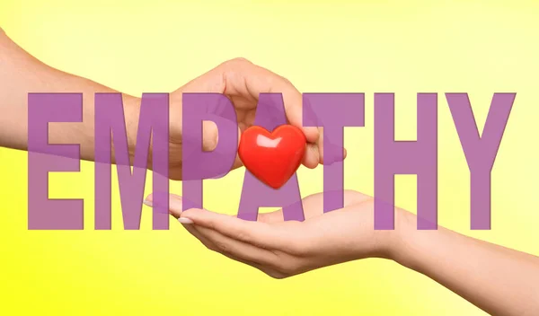 Empathy. Man giving heart to woman as symbol of emotional support on yellow background, closeup