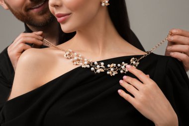 Man putting elegant necklace on beautiful woman against grey background, closeup clipart