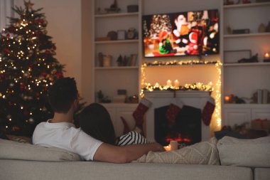 Çift, rahat bir odada televizyon izleyerek Noel filmi izliyor. Kış tatili atmosferi