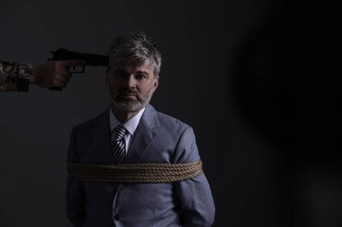 Kidnapper aiming gun at tied victim on dark background, space for text. Hostage taking
