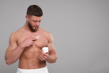 Yakışıklı adam göğsüne açık gri arka planda vücut kremi sürüyor, mesaj için yer var.
