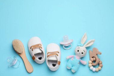 Flat lay composition with pacifiers and other baby stuff on light blue background. Space for text