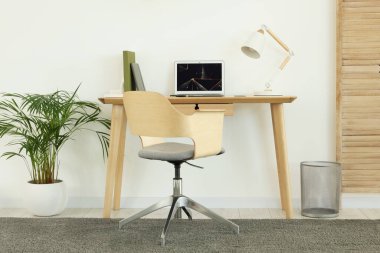 Cozy workspace with modern laptop on desk and comfortable chair at home