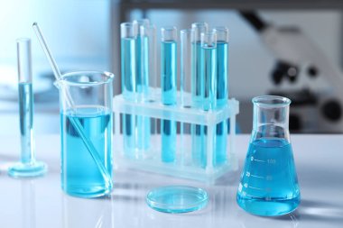 Laboratuvardaki masada açık mavi sıvı bulunan farklı cam eşyalar ve test tüpleri.