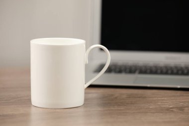 Beyaz seramik bardak ve laptop iş yerindeki ahşap masada. Metin için boşluk