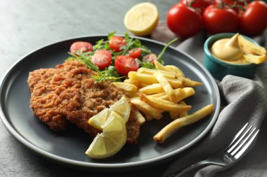 Patates kızartması, domates ve roka ile servis edilen lezzetli şnitzeller gri masada, yakın plan.
