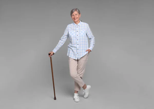 stock image Senior woman with walking cane on gray background