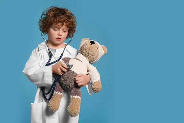 Mały Chłopiec Mundurze Medycznym Badający Pluszowego Misia Stetoskopem Jasnoniebieskim Tle — Zdjęcie stockowe