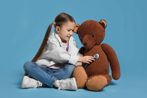 Dziewczynka Mundurze Medycznym Badająca Misia Zabawki Stetoskopem Jasnoniebieskim Tle — Zdjęcie stockowe