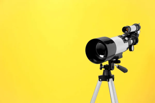 Tripod with modern telescope on yellow background, closeup. Space for text