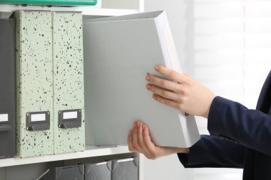 Woman taking folder with documents from shelf in office, closeup