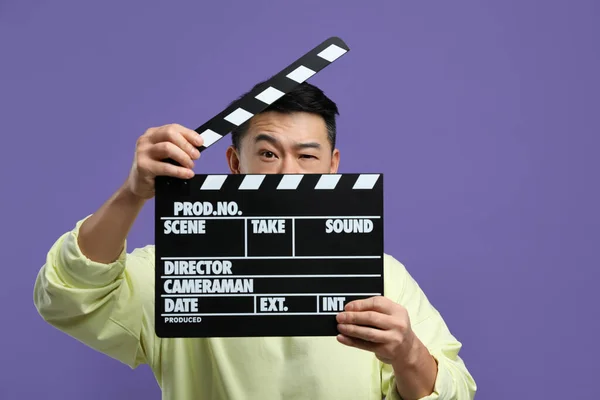 Asian actor with clapperboard on purple background. Film industry
