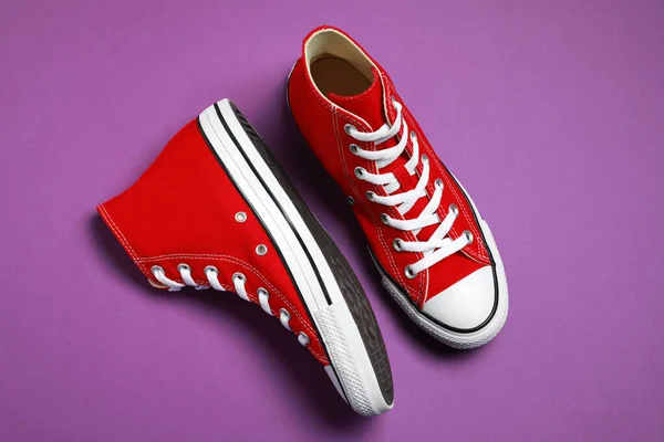 Pair of new stylish red sneakers on purple background, flat lay