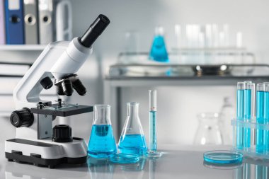 Farklı laboratuvar camları, üzerinde açık mavi sıvı ve mikroskop bulunan test tüpleri.