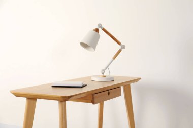 Modern masa lambası ve beyaz duvarın yanındaki ahşap masa üzerindeki kitaplar.