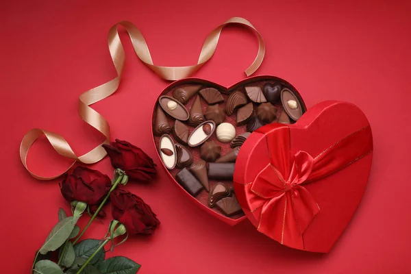 Herzförmige Schachtel Mit Leckeren Schokoladenbonbons Rosen Und Schleife Auf Rotem — Stockfoto