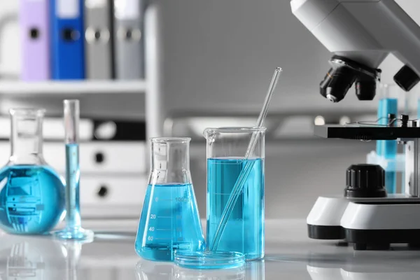 テーブルの上に顕微鏡の近くにライトブルーの液体と異なる研究室のガラス製品 — ストック写真