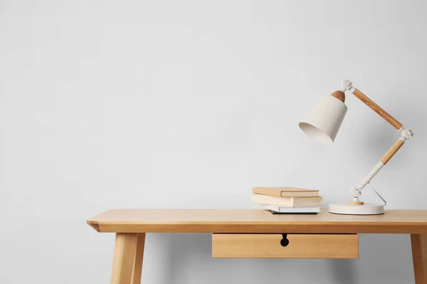 Stylish modern desk lamp and books on wooden table near white wall