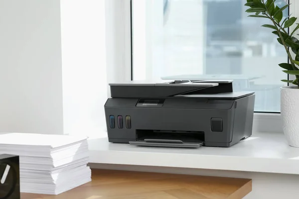 在窗台附近的木制桌子上堆放着一堆堆纸 办公室里有现代打印机 — 图库照片