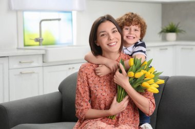 Anneler Günü 'nde annesini tebrik eden küçük bir çocuk. Sarı lale buketi tutan kadın.