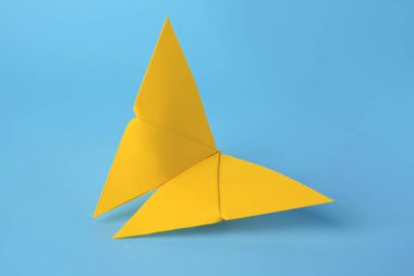 Origami sanatı. Açık mavi arkaplanda el yapımı sarı kağıt kelebek