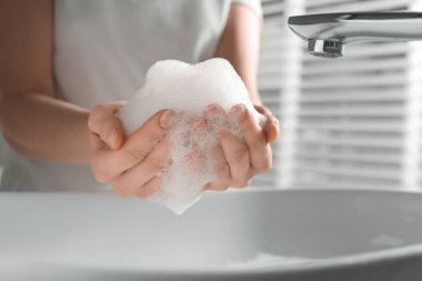 Woman washing hands with cleansing foam near sink in bathroom, closeup