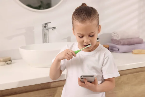Κοριτσάκι Που Χρησιμοποιεί Smartphone Ενώ Βουρτσίζει Δόντια Στο Μπάνιο Χώρο — Φωτογραφία Αρχείου