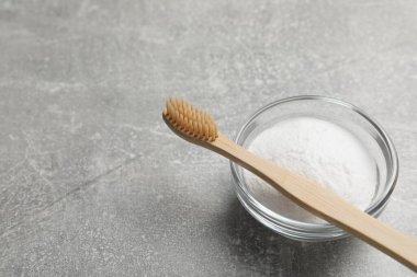 Bambu diş fırçası ve gri masada bir kase kabartma tozu, metin için yer.