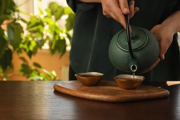 女人在室内的木制桌子上 把刚泡好的茶从茶壶倒进杯子里 这是特写镜头和文字空间 传统仪式 — 图库照片