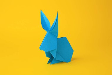 Origami sanatı. Sarı arkaplanda el yapımı açık mavi kağıt tavşan, yakın plan.