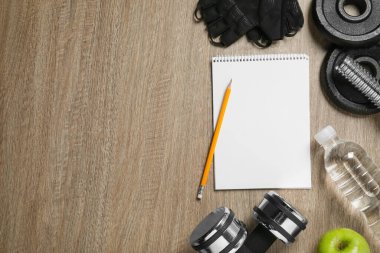 Defter, kalem ve spor aletleri ahşap masada, düz yerde, yazı için yer var. Kişisel eğitim