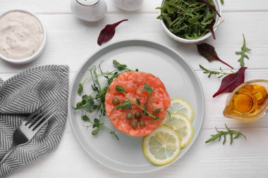 Beyaz ahşap masada servis edilen limonlu, kapari ve mikro yeşillikli lezzetli somon tartar.