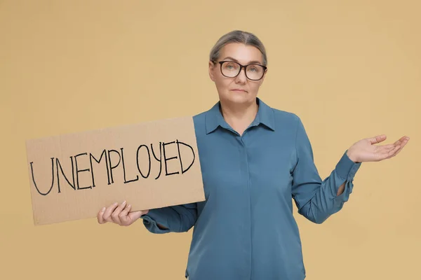 Verwirrte Seniorin Hält Pappschild Mit Wort Arbeitslos Auf Beigem Hintergrund — Stockfoto