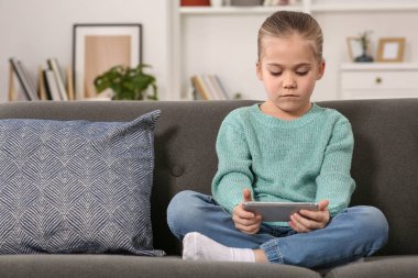 Evdeki kanepede akıllı telefon kullanan küçük bir kız. İnternet bağımlılığı