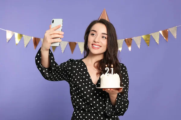 年齢層のパーティー 21歳の誕生日 笑顔の女性保持おいしいケーキとともに数形のキャンドルと取ります自己撮影バイオレット背景 — ストック写真