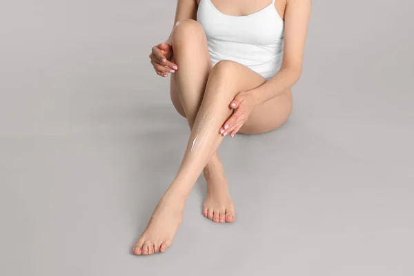 Donna Che Applica Crema Corpo Sulle Gambe Lisce Sfondo Grigio — Foto Stock