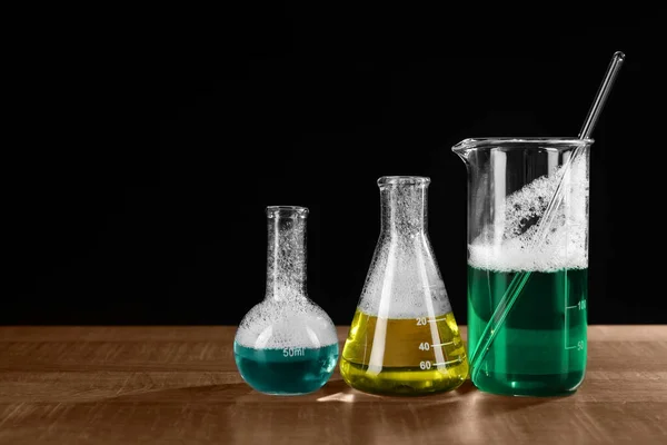实验室玻璃器皿 木制桌子上有五颜六色的液体 背景为黑色 空间为文字 化学反应 — 图库照片