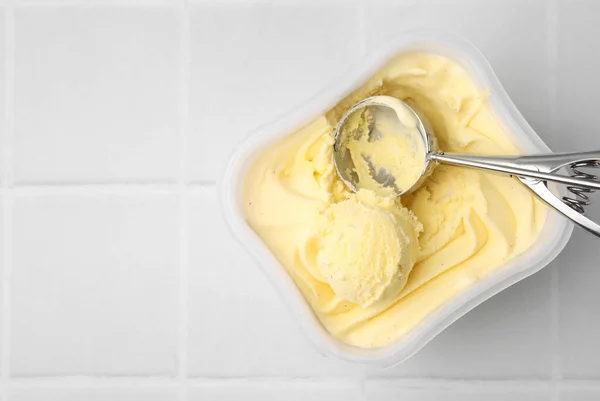 Vanilla ice cream and scoop in container on white tiled table, top view. Space for text