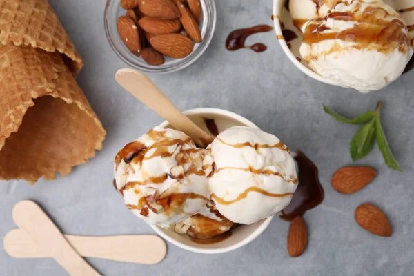 stock image Scoops of ice cream with caramel sauce and nuts on light grey table, flat lay