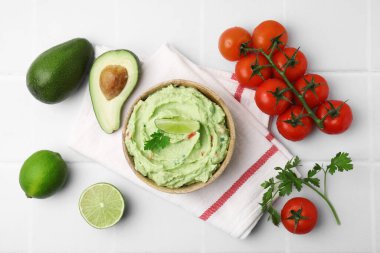 Bir kase lezzetli guacamole ve malzemeler beyaz fayanslı masada, düz yerde.