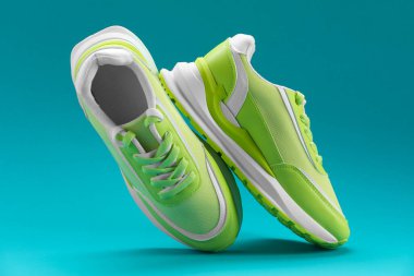Bir çift şık yeşil spor ayakkabısı, deniz mavisi zemininde uçuyor.