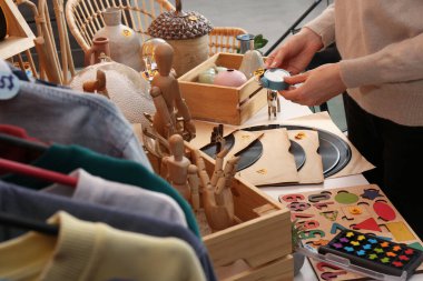 Masanın yanında bir sürü farklı eşyası olan alarmlı saati tutan kadın, yakın plan. Garaj satışı