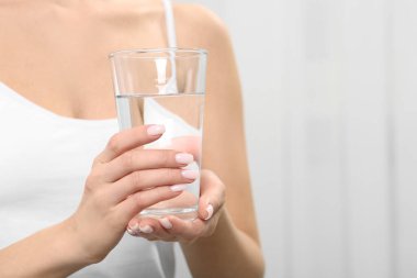 Sağlıklı alışkanlık. Kapalı mekanda su dolu cam bardakları tutan kadına yakın çekim.