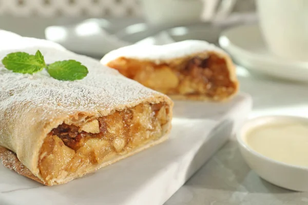 Delicious strudel with apples, nuts and powdered sugar on table, closeup. Space for text