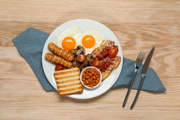 揚げ卵とプレート ソーセージ キノコ 木製のテーブルの上にベーコンとトースト 平置き 伝統的な英語の朝食 — ストック写真