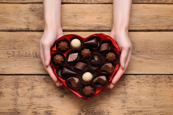 女人抱着心形的盒子 在木制桌子旁放着美味的巧克力糖果 俯瞰全景 — 图库照片