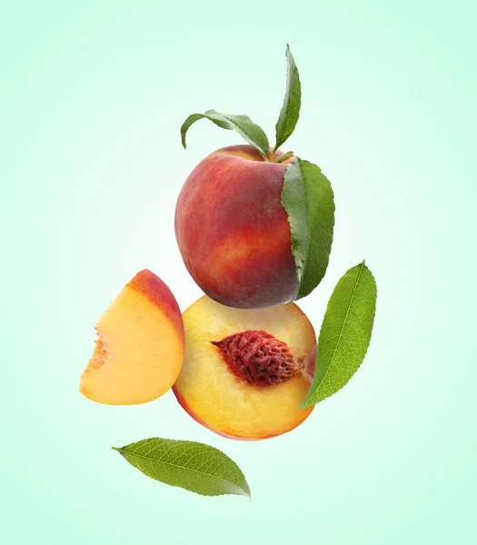 stock image Juicy fresh peaches with green leaves falling on light turquoise background