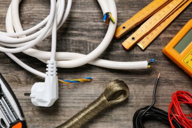 Wires and electrician's tools on wooden table, flat lay